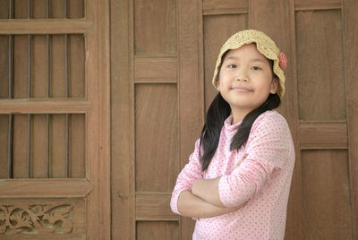 Portrait of smiling girl standing against wooden wall