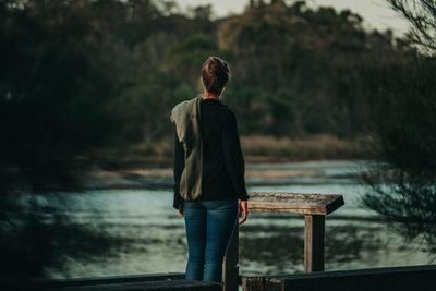 Rear view of woman standing on pier over lake