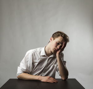 Young man looking away while sitting against wall