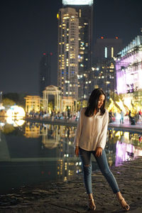 Full length of woman standing against illuminated buildings in city at night