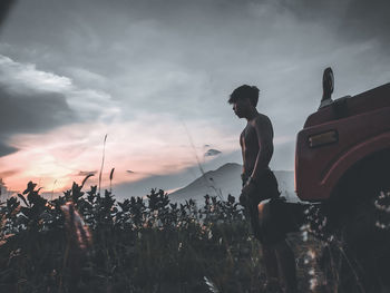 Woman standing by plants against sky during sunset