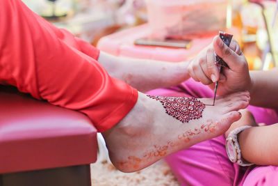 Cropped image of beautician making henna tattoo on bride leg