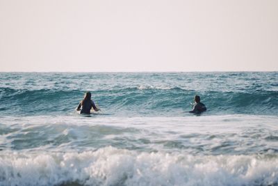 People swimming in sea against clear sky