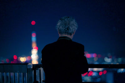 Rear view of man standing against illuminated city at night