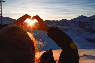 Rear view of woman making heart shape against sun during sunset