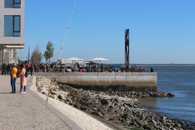 People standing on shore by sea against clear sky