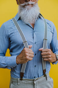 Midsection of man holding umbrella against yellow background