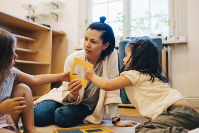 Female teacher and students holding picture frame while sitting in classroom at child care