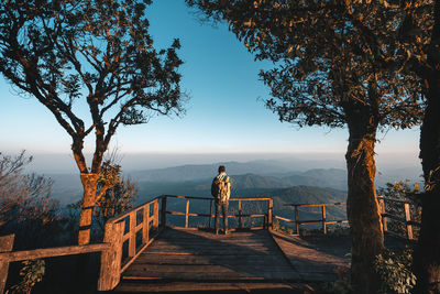 Rear view of man standing by railing against sky