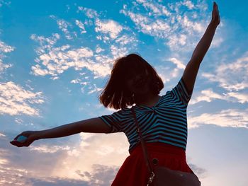 Rear view of woman with arms raised standing against sky