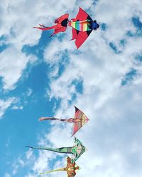 Low angle view of colorful kites flying against cloudy sky