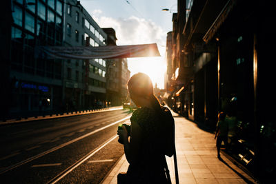 Rear view of mid adult woman photographing while standing on sidewalk in city