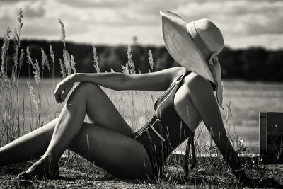 A woman in a swimsuit, hat and sunglasses sunbathes in summer on the riverbank among the grass