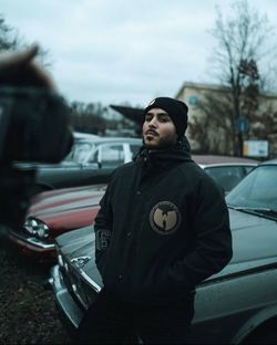 Portrait of young man standing against car