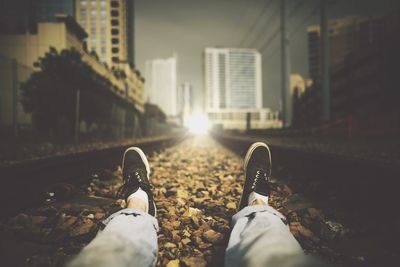 Cropped image of man sitting on railroad track at night