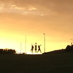 Silhouette people playing on field against sky during sunset