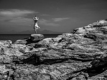 Man standing on rock by sea against sky