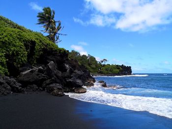 Scenic view of rocks on black volcanic beach against sky