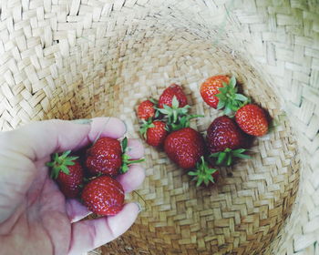 Cropped hand of woman holding strawberry over straw hat