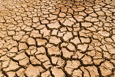 Dry cracked orange stony soil, top view.