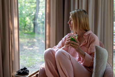 A woman drinks herbal tea in the living room and looks out the window.