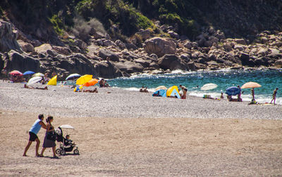 People walking at beach against rocks