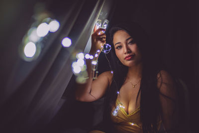 Portrait of beautiful woman holding illuminated lights at night