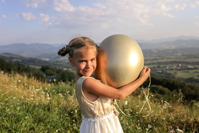 Boy standing on balloon at field against sky