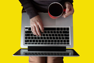 Midsection of woman using laptop while holding coffee cup