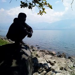 Man sitting on rock by sea against sky