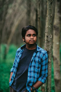 Portrait of young man standing against trees in forest