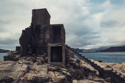 Old ruin building by sea against cloudy sky