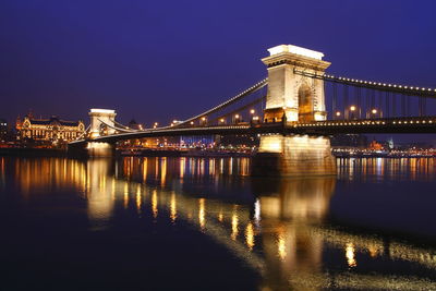 Illuminated bridge over river against sky at night