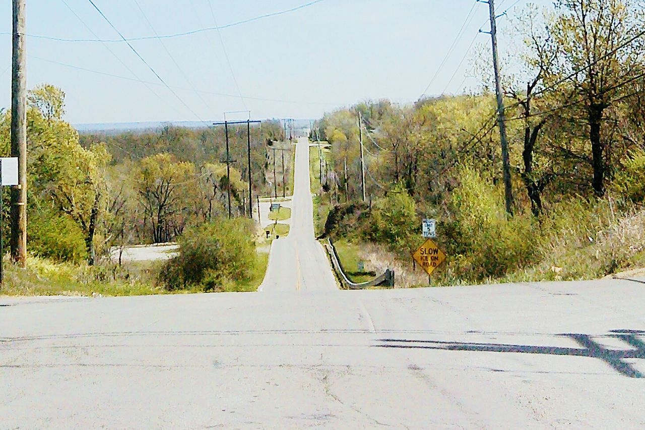 tree, the way forward, built structure, power line, road, architecture, transportation, clear sky, building exterior, street, house, electricity pylon, growth, day, sky, plant, outdoors, no people, diminishing perspective, nature