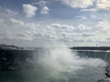 Scenic view of waterfall against cloudy sky