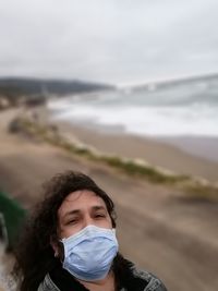 Portrait of man on beach against sky with mask