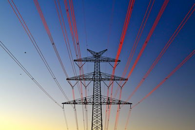 Low angle view of electricity pylon against sky during sunset