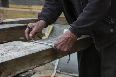 Midsection of carpenter measuring wood while working in carpentry workshop