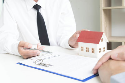 Midsection of real estate agent and client discussing over contract on table