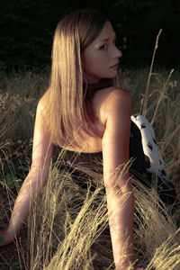 Rear view of beautiful woman sitting on field during sunset