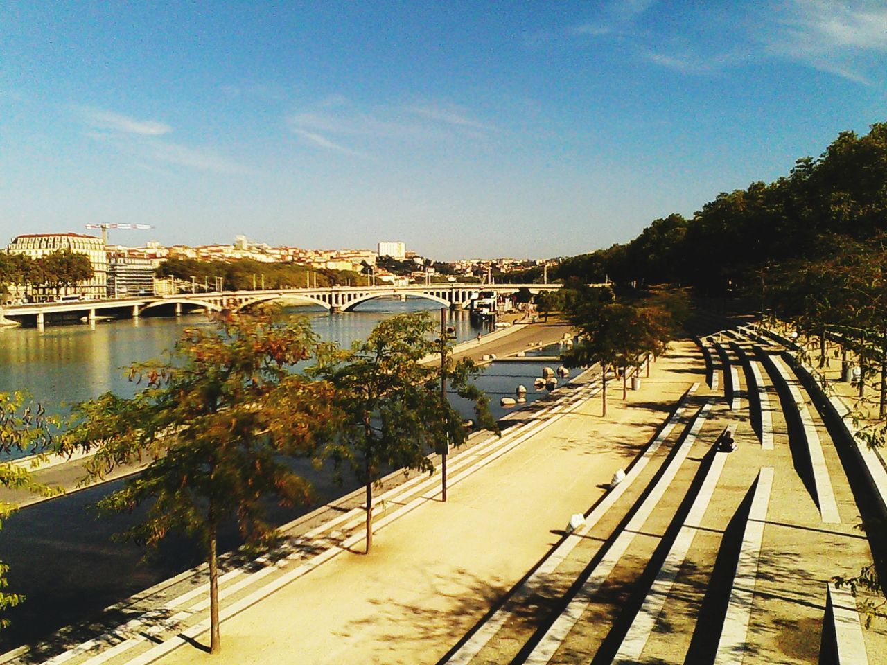 built structure, architecture, water, sky, building exterior, tree, the way forward, railing, river, bridge - man made structure, pier, sunlight, city, connection, outdoors, incidental people, day, walkway, shadow, nature