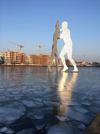 Statue by water in city against clear sky