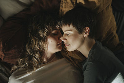 Directly above shot of lesbian couple lying face to face on bed at home