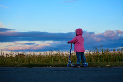 Girl standing with push scooter against cloudy sky
