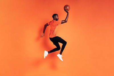 Full length of man jumping against orange background