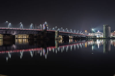 Illuminated bridge over river against sky at night