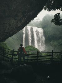 Man standing by railing against waterfall