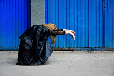 Full length of woman posing against corrugated wall on footpath