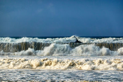 Scenic view of sea with crashing waves against clear blue sky