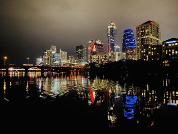 Illuminated buildings by river against sky at night